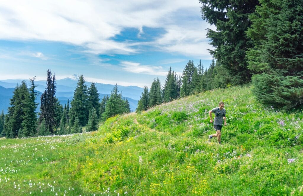 trail runner running along a single-track dirt trail through a field of grasses and wildflowers